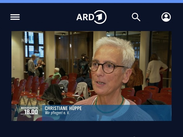 Das Bild ist ein Screenshot von der Webseite der ARD Mediathek. ZU sehen ist ein Standbild aus einem Filmbeitrag des NDR zur Woche der pflegenden Angehörigen in Niedersachsen 2025. Zu sehen ist Christiane Hüppe, Vorständen des Vereins wir pflegen in Niedersachsen e.V., die gerade ein Interview gibt. Sie schaut seitlich in die Kamera. Sie trägt eine Brille und hat kurze Haare. Im Hintergrund sind Stuhlreihen und einige Menschen zu sehen, die sich unterhalten.