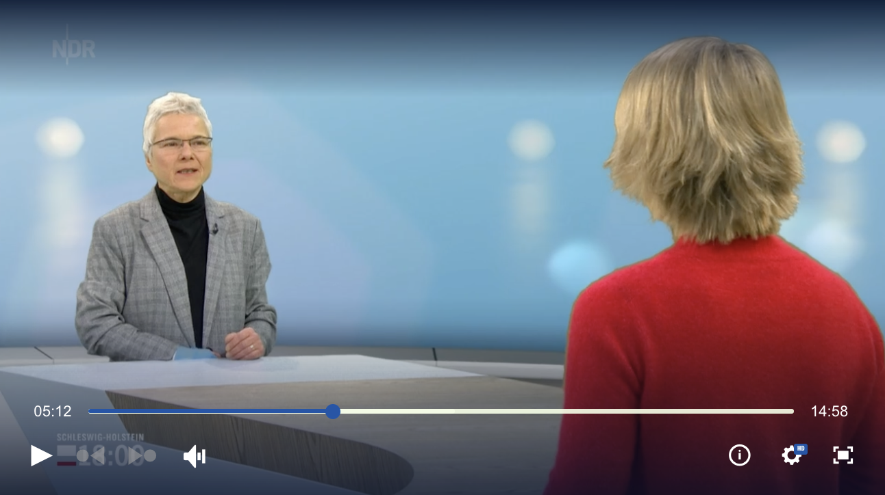 Auf dem Bild ist ein Filmausschnitt des Interviews mit Frau Knudsen zu sehen. Zu sehen ist das NDR Studio. Frau Knudsen ist links im Bild und spricht gerade. Rechts im Bild ist die Moderatorin von hinten zu sehen. 